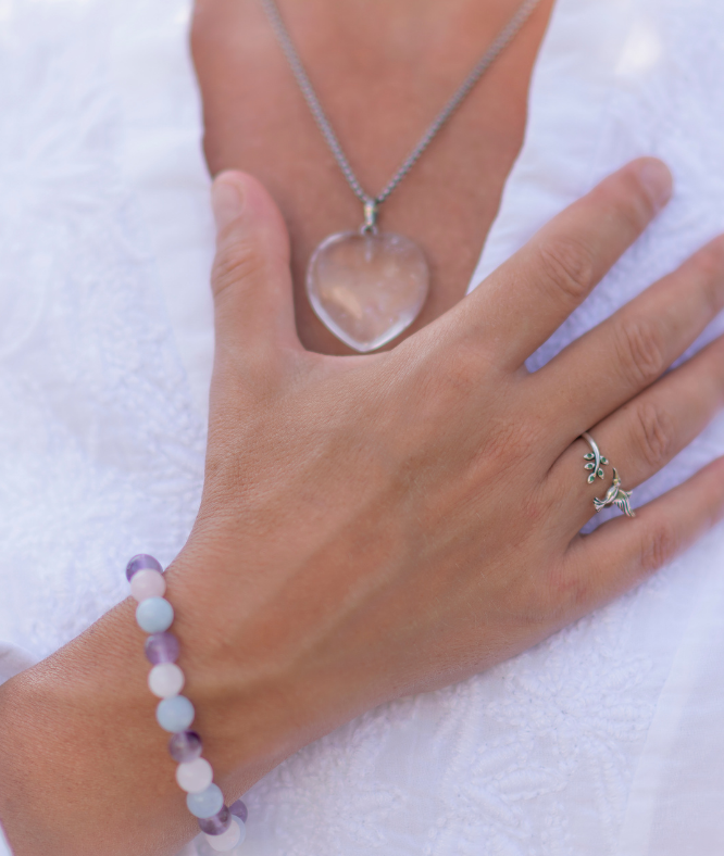 Frau legt Hand auf ihr Herz und trägt einen herzförmigen Anhänger und einem Ring, daneben ein Armband.