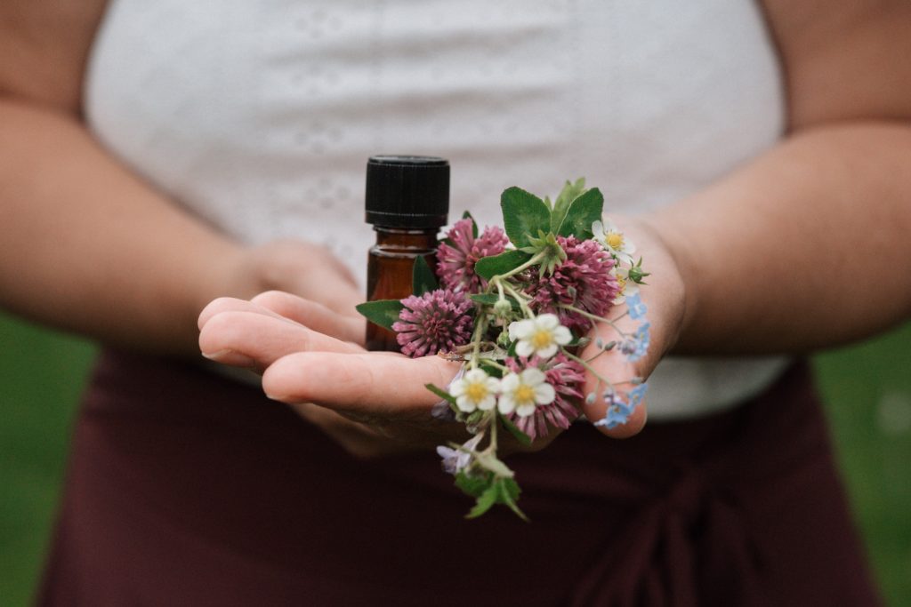 Aromapraxis: Aromaberatung, Begleitung & Massagen Eine Hand hält eine kleine Flasche und buntes Pflanzenmaterial.