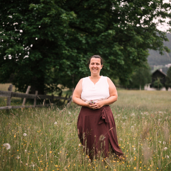 Mein Blog für DICH! Frau im weißen Oberteil und brauem Rock steht in einer blühenden Wiese vor einem Baum.